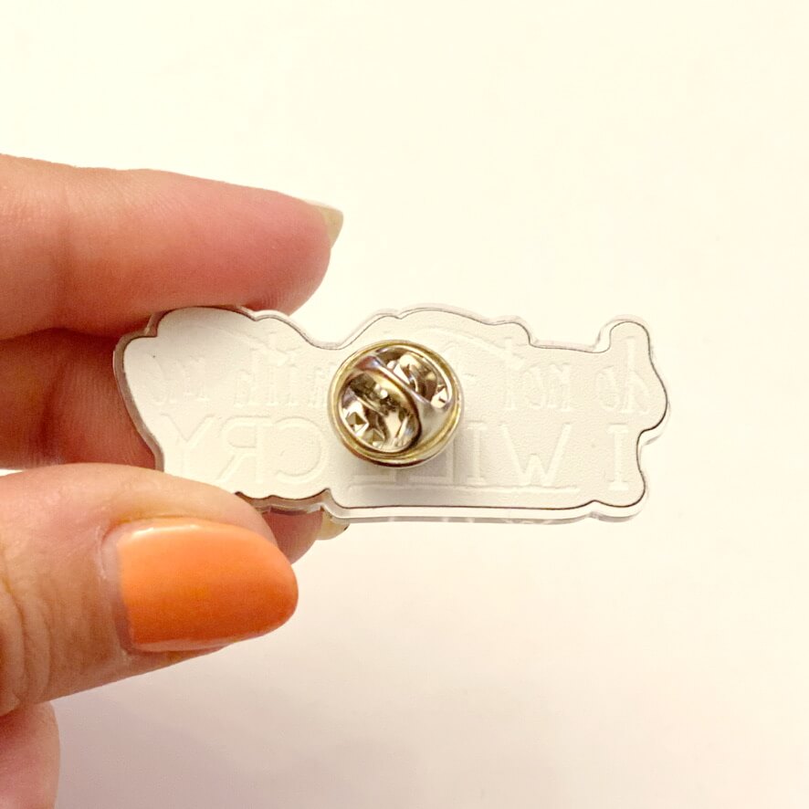 Close up of fingers holding an I will cry pin showing the back