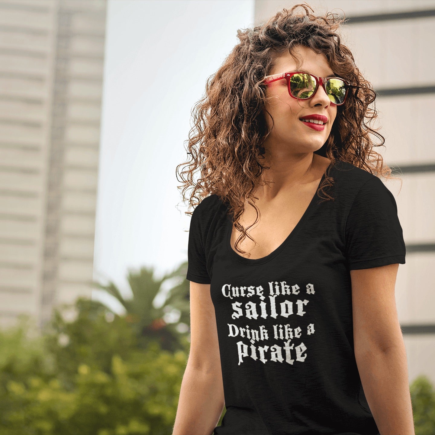 Woman with dark curly hair wears a black t-shirt with the words curse like a sailor drink like a pirate in white.