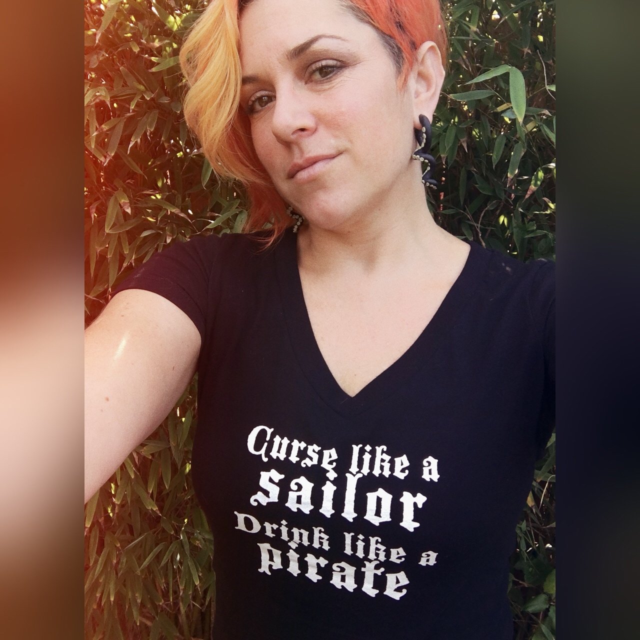 Orange haired woman in v-neck black t-shirt that says "Curse like a sailor drink like a pirate"