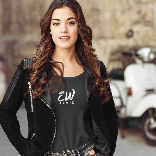 woman with long dark hair wearing an "Ew David" short sleeve t-shirt with black jeans and a black jacket unzipped