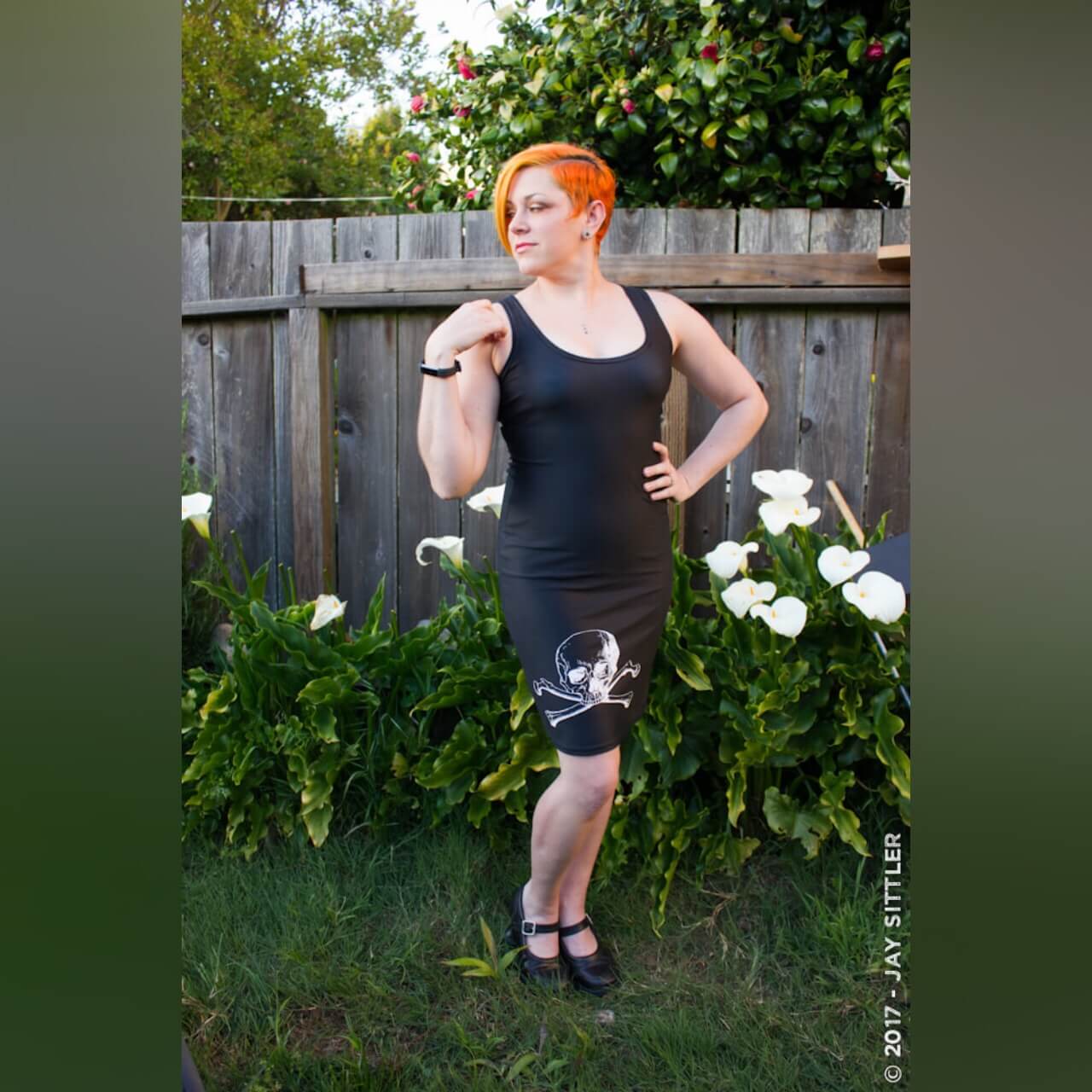 Woman with orange hair wearing black skull and crossbones pencil dress outside
